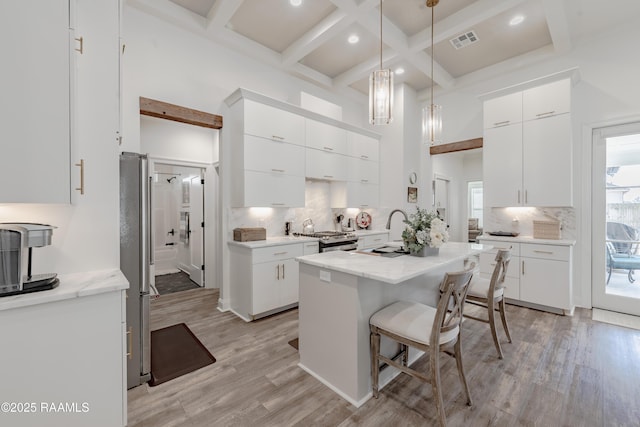 kitchen featuring white cabinetry, sink, a high ceiling, coffered ceiling, and light wood-type flooring