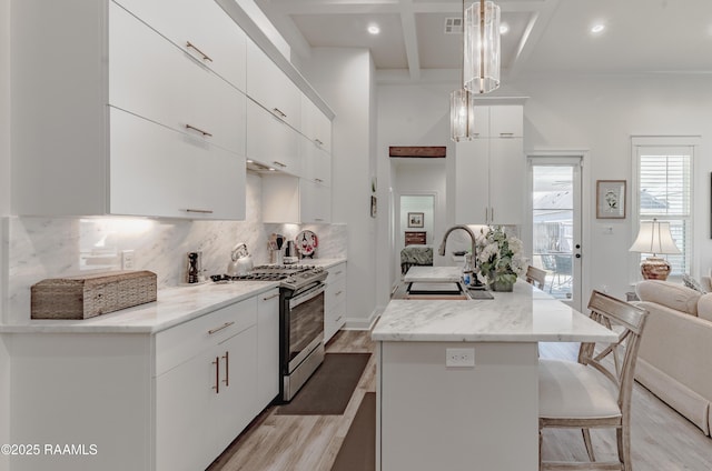 kitchen with hanging light fixtures, white cabinetry, sink, and stainless steel gas range