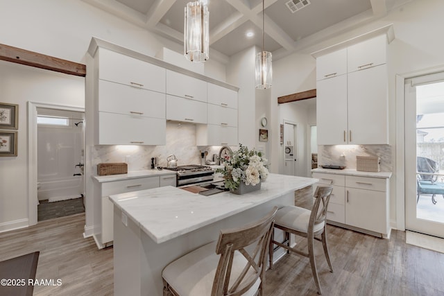 kitchen with white cabinetry, hanging light fixtures, stainless steel gas stove, and light hardwood / wood-style floors