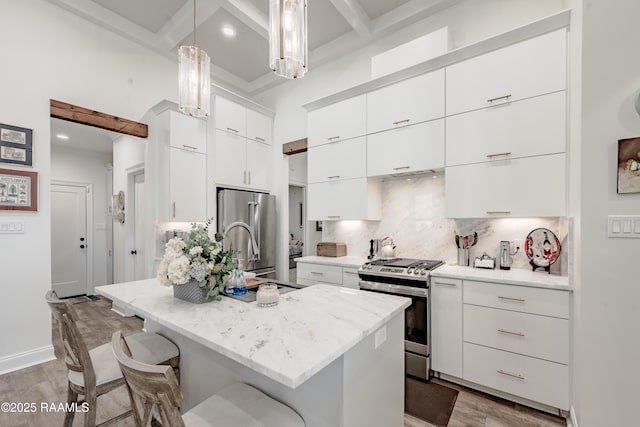 kitchen featuring pendant lighting, white cabinetry, stainless steel appliances, tasteful backsplash, and an island with sink