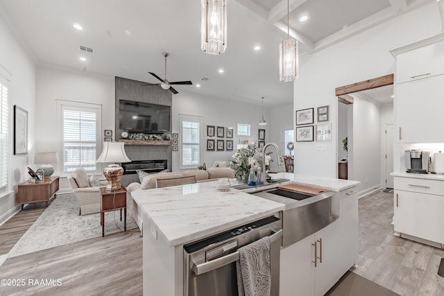 kitchen with pendant lighting, dishwasher, white cabinetry, a large fireplace, and a center island with sink