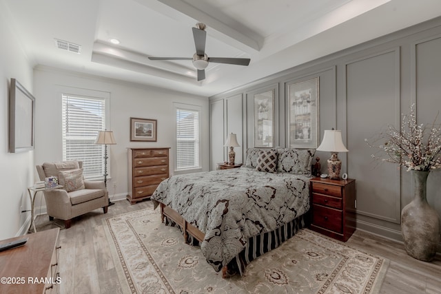 bedroom featuring ornamental molding, ceiling fan, light wood-type flooring, and a tray ceiling