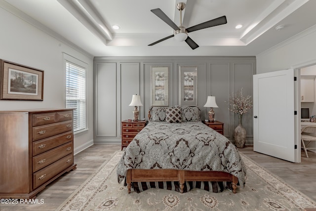 bedroom featuring crown molding, ceiling fan, a tray ceiling, and light hardwood / wood-style flooring