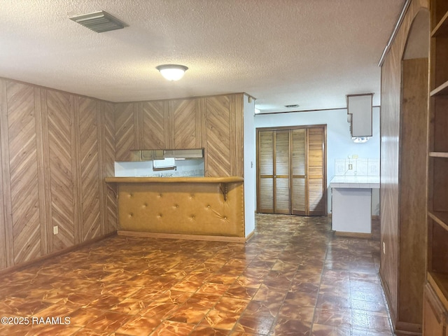 kitchen with kitchen peninsula, a textured ceiling, and wood walls