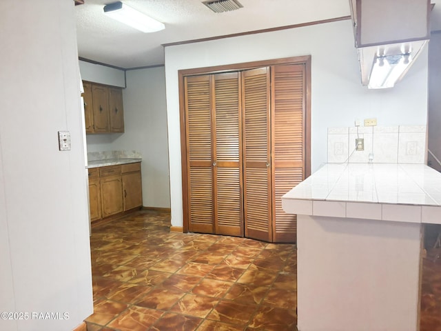 kitchen with crown molding, tile countertops, kitchen peninsula, and a textured ceiling