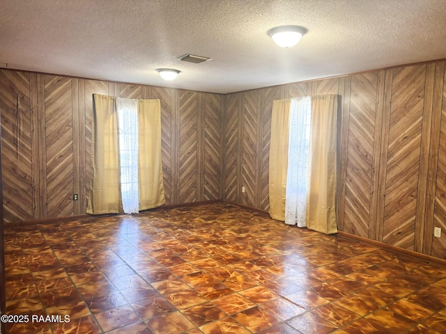 empty room featuring a textured ceiling and wood walls