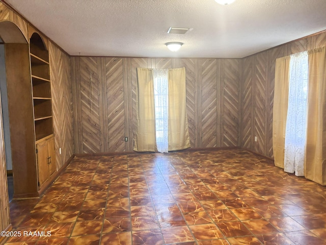 unfurnished room with wooden walls and a textured ceiling