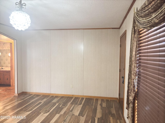 spare room featuring a notable chandelier, crown molding, a textured ceiling, and dark hardwood / wood-style flooring