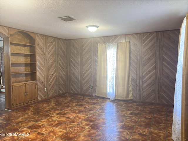 unfurnished room featuring a textured ceiling and wood walls