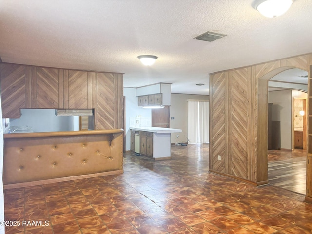 kitchen with white cabinets, kitchen peninsula, a textured ceiling, and wood walls