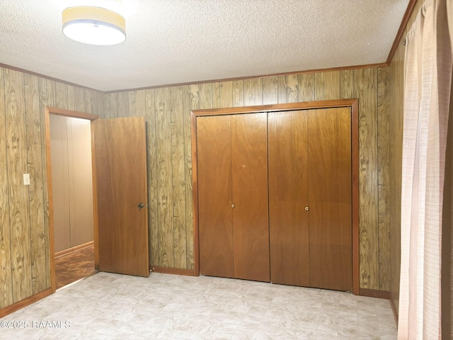 unfurnished bedroom with ornamental molding, wood walls, a textured ceiling, and a closet