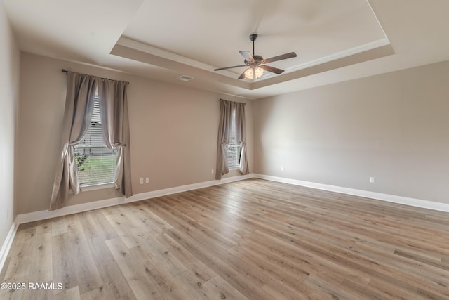 empty room featuring a raised ceiling, ornamental molding, and light wood-type flooring