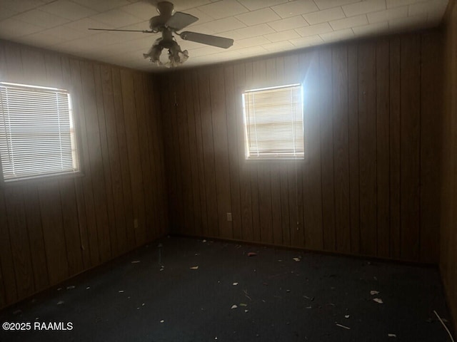 unfurnished room featuring ceiling fan and wood walls