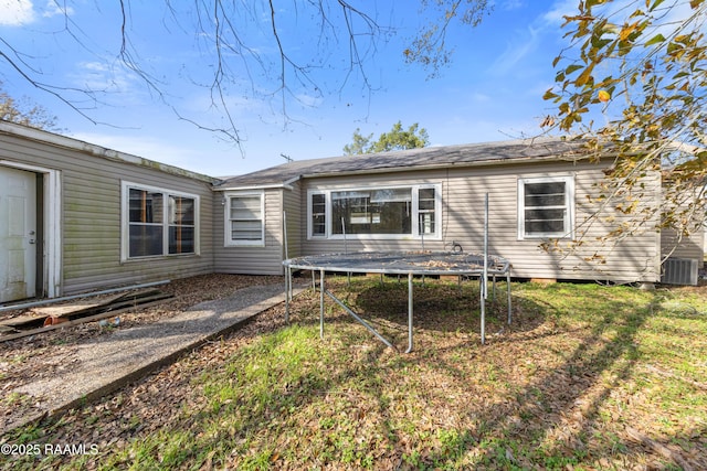 rear view of house featuring a yard, central AC, and a trampoline