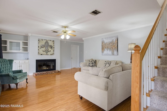 living room featuring hardwood / wood-style floors, a fireplace, ornamental molding, and ceiling fan