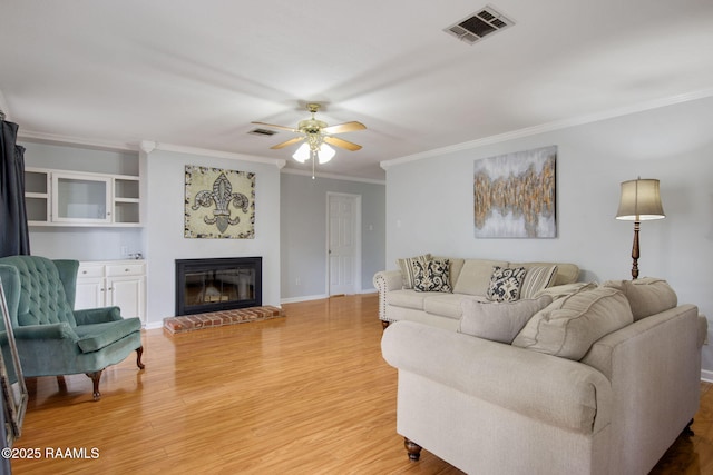 living room featuring hardwood / wood-style flooring, ceiling fan, ornamental molding, and a fireplace