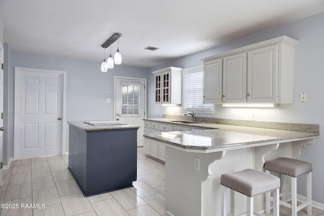 kitchen featuring a kitchen island, white cabinetry, sink, hanging light fixtures, and kitchen peninsula