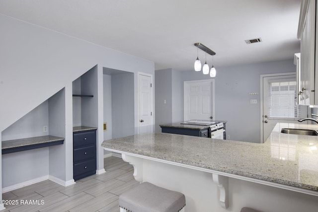 kitchen featuring built in desk, blue cabinets, sink, stainless steel range, and kitchen peninsula