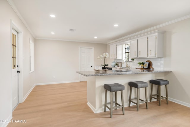 kitchen featuring white cabinetry, crown molding, light hardwood / wood-style floors, and decorative backsplash