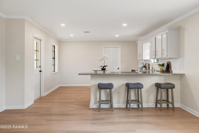 kitchen with light stone counters, kitchen peninsula, light wood-type flooring, and white cabinets