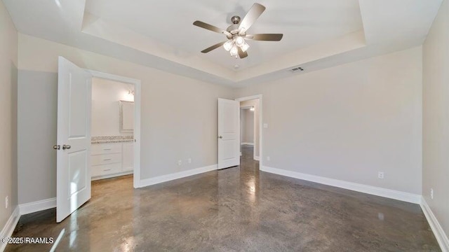 unfurnished bedroom with ceiling fan, ensuite bathroom, and a raised ceiling