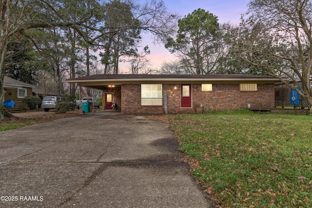 single story home featuring brick siding, a lawn, an attached carport, and driveway