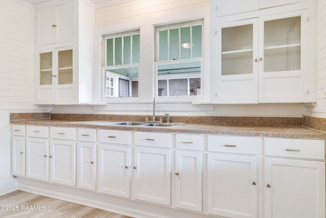 kitchen featuring sink, light hardwood / wood-style flooring, white cabinets, and wood walls