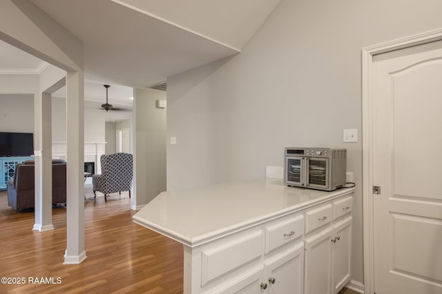 kitchen with light wood-style flooring, a peninsula, a fireplace, white cabinetry, and light countertops