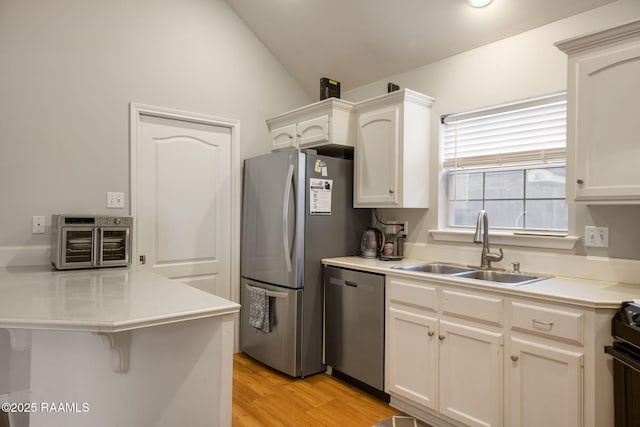 kitchen featuring stainless steel appliances, light countertops, a sink, a peninsula, and a kitchen bar