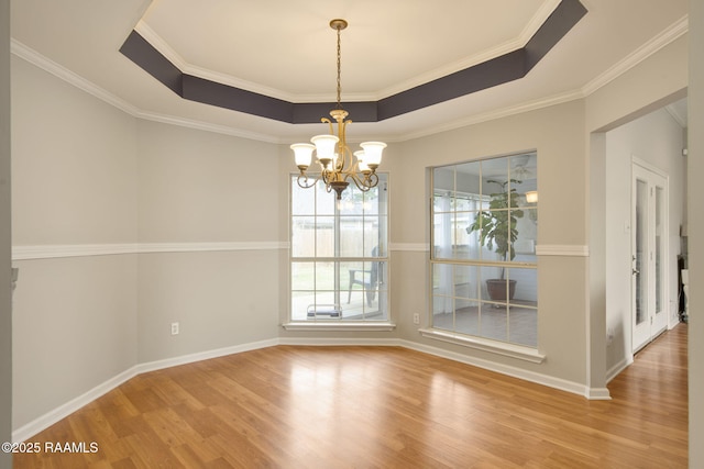 unfurnished dining area featuring a tray ceiling, ornamental molding, wood finished floors, a chandelier, and baseboards