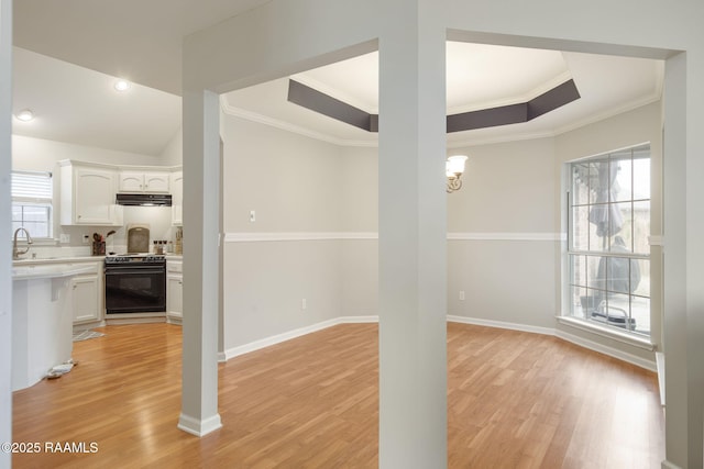 unfurnished dining area with light wood-style floors, crown molding, a sink, and baseboards