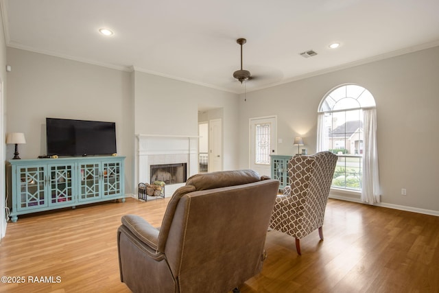 living room with ornamental molding, light wood-type flooring, visible vents, and a tile fireplace