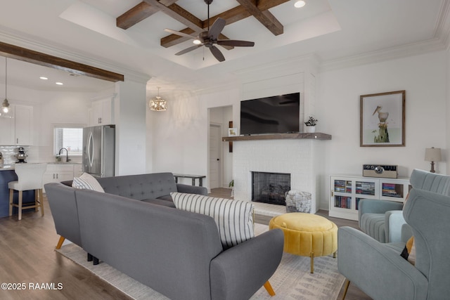 living room with sink, light wood-type flooring, coffered ceiling, a brick fireplace, and beam ceiling