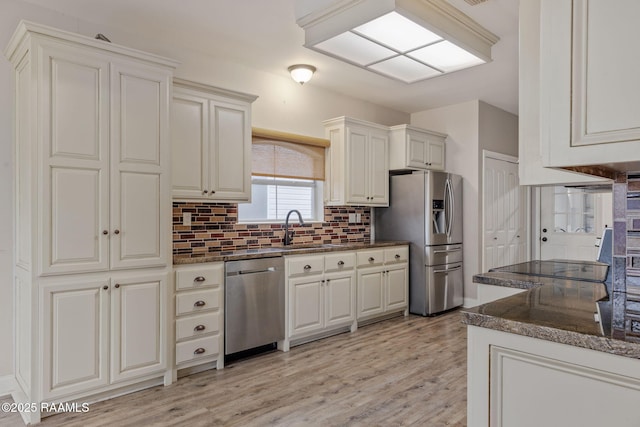 kitchen featuring dark stone counters, stainless steel appliances, light hardwood / wood-style floors, decorative backsplash, and white cabinets