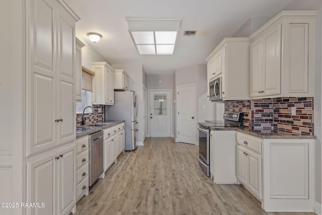 kitchen with sink, stainless steel appliances, light hardwood / wood-style floors, white cabinets, and decorative backsplash