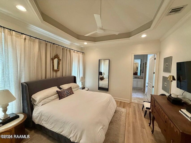 bedroom featuring ensuite bath, light hardwood / wood-style flooring, ceiling fan, a tray ceiling, and ornamental molding