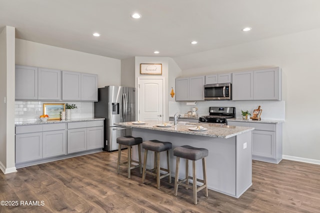 kitchen featuring an island with sink, a breakfast bar, wood finished floors, gray cabinets, and stainless steel appliances