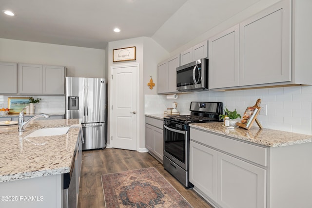 kitchen with light stone counters, dark wood-style flooring, a sink, appliances with stainless steel finishes, and backsplash