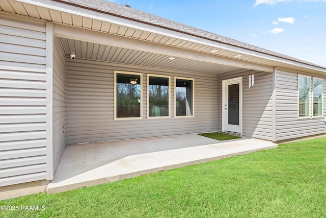 doorway to property featuring a yard, a shingled roof, and a patio