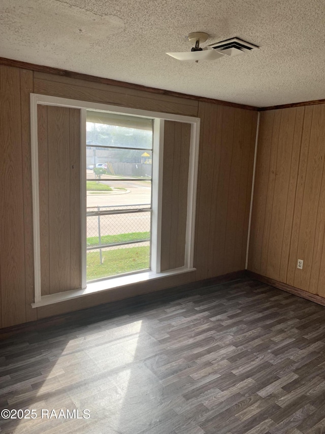 spare room featuring dark wood-type flooring, wooden walls, and a textured ceiling