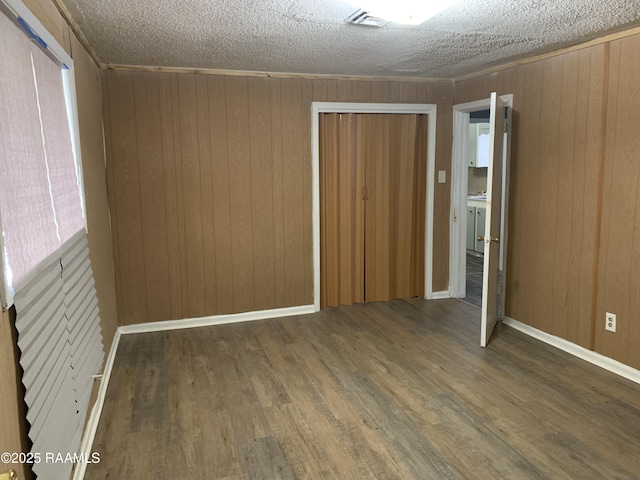 empty room with ornamental molding, dark wood-type flooring, wooden walls, and a textured ceiling