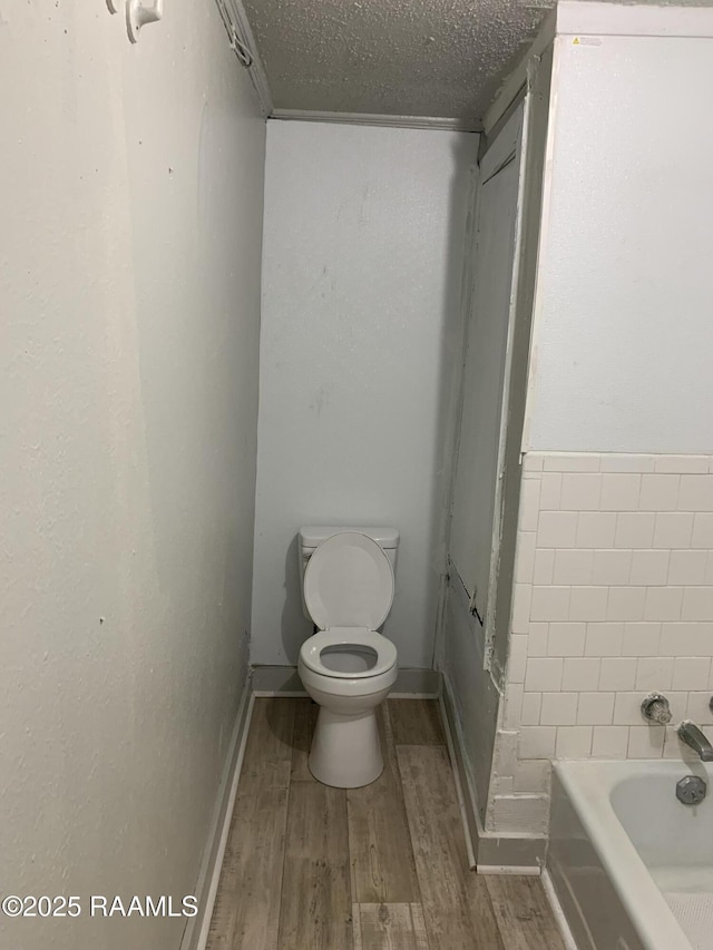 bathroom featuring wood-type flooring, a tub, a textured ceiling, and toilet