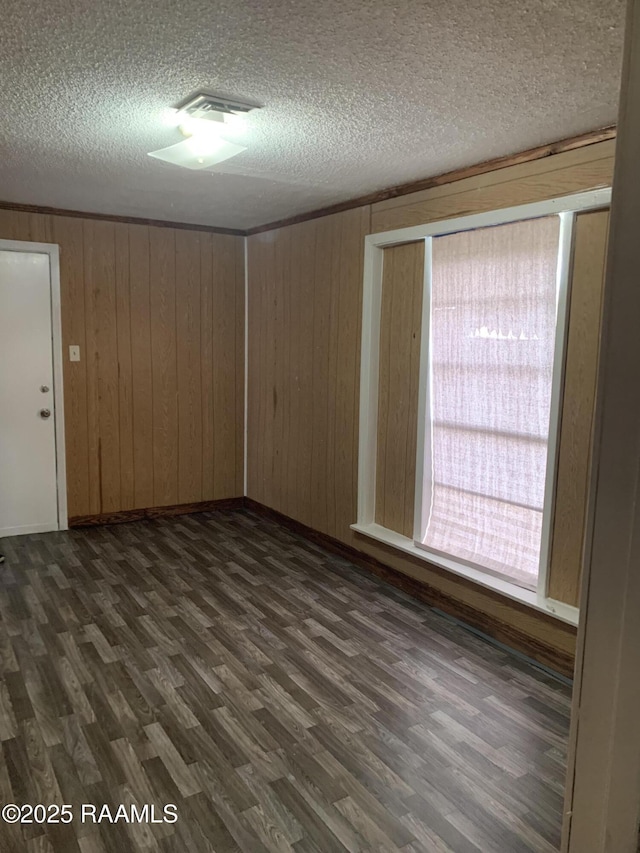 empty room with dark wood-type flooring, a textured ceiling, and wood walls