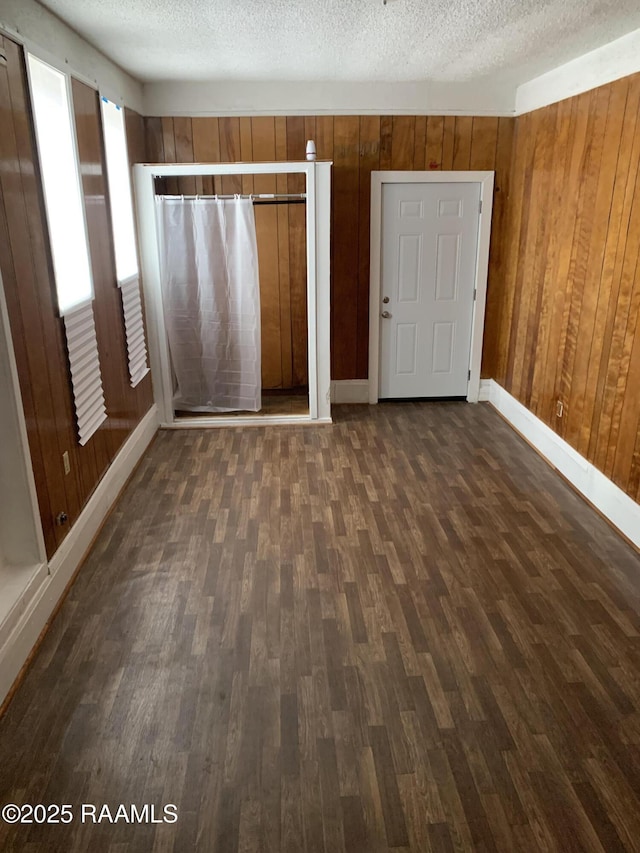 unfurnished bedroom featuring dark wood-type flooring, a textured ceiling, and wood walls