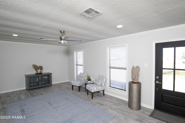 living area with ornamental molding, a healthy amount of sunlight, wood-type flooring, and a textured ceiling