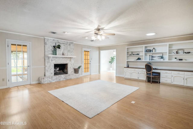 unfurnished living room featuring crown molding, a fireplace, built in desk, light hardwood / wood-style floors, and a textured ceiling