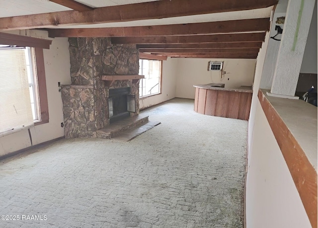 unfurnished living room featuring beam ceiling, a stone fireplace, a wall unit AC, and light colored carpet