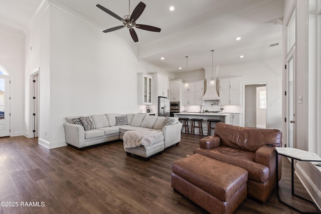 living room featuring crown molding, dark hardwood / wood-style floors, ceiling fan, and a towering ceiling