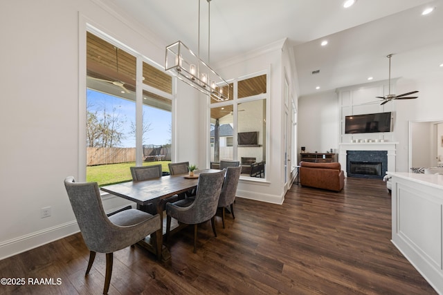 dining room with ceiling fan with notable chandelier, a fireplace, and dark hardwood / wood-style floors