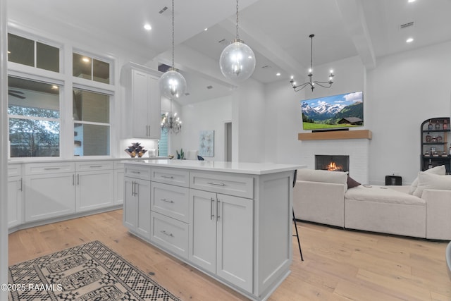 kitchen with light wood-type flooring, a kitchen island, open floor plan, white cabinetry, and a brick fireplace